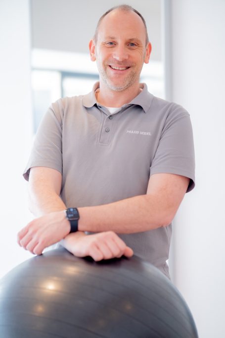 Lächelnder Mann in Sportkleidung, der an einem Fitnessball steht.