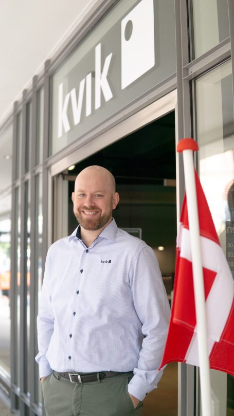 Lächelnder Mann vor dem Eingang eines Geschäftes mit dänischer Flagge.